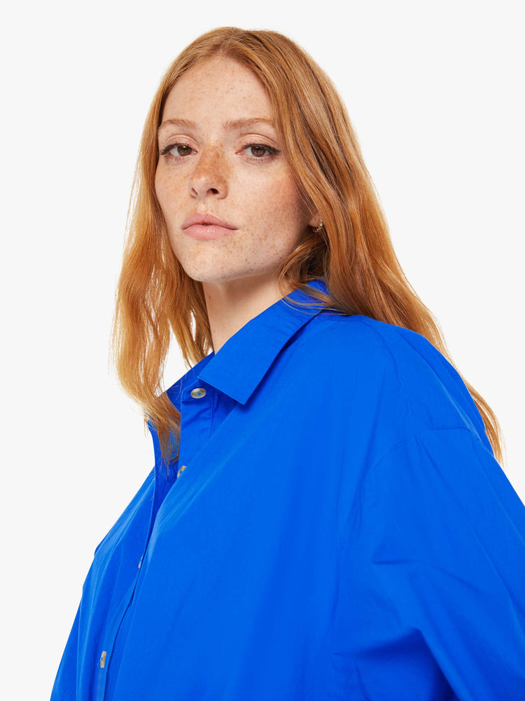 Close up view of a woman royal blue lightweight collared jumpsuit with longsleeves, a tied waist, cargo patch pockets and an ankle-length straight leg.