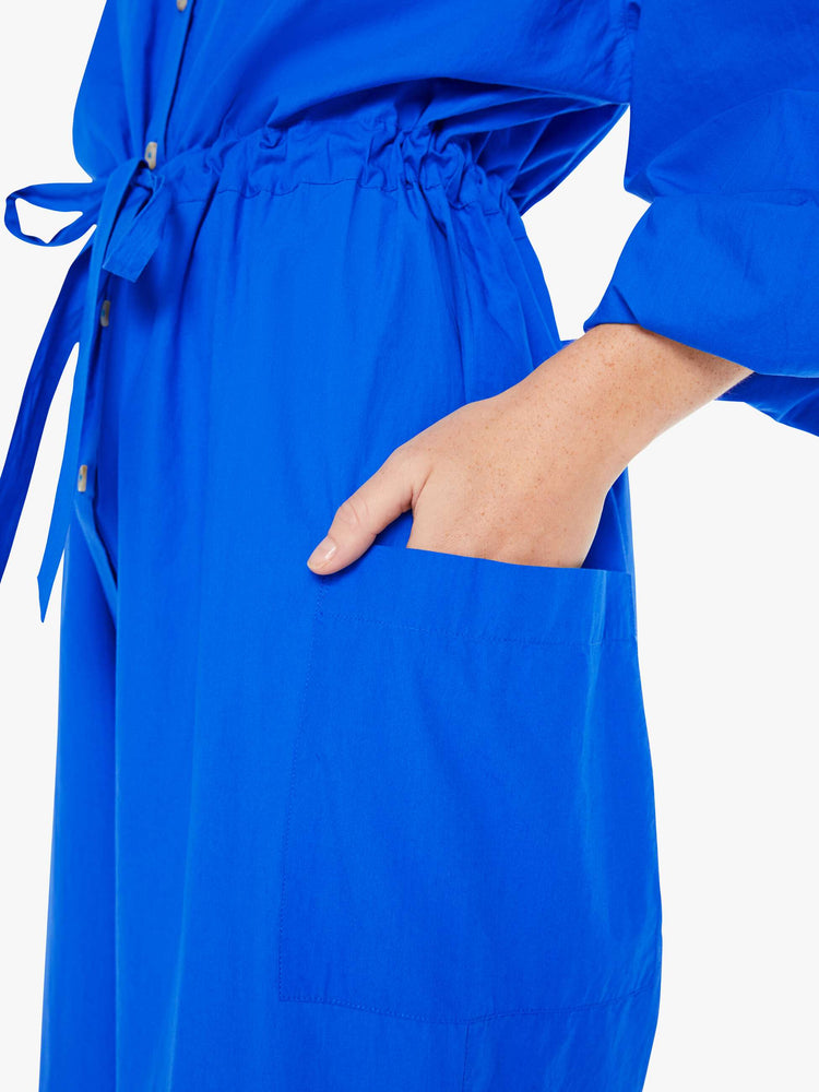Close up view of a woman royal blue lightweight collared jumpsuit with longsleeves, a tied waist, cargo patch pockets and an ankle-length straight leg.