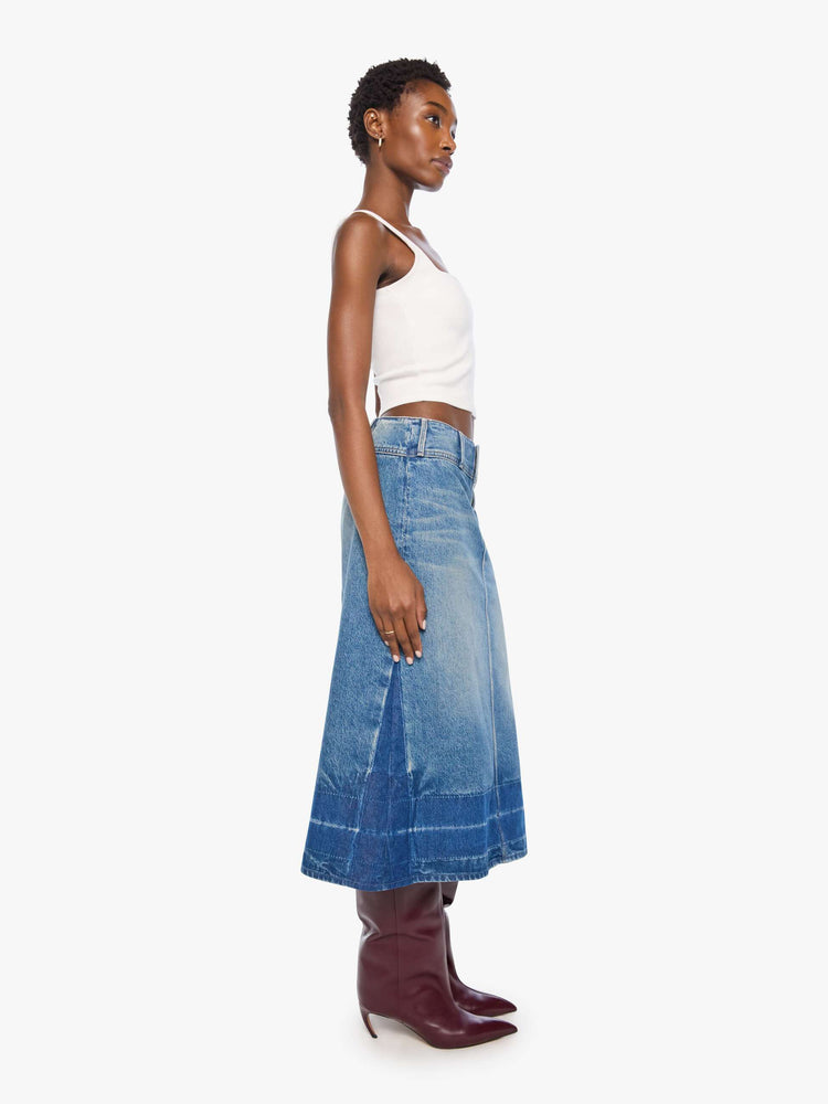 Side view of a woman in a mid blue skirt is designed with an extra-wide waistband, zip closure, A-line fit and an undone hem.
