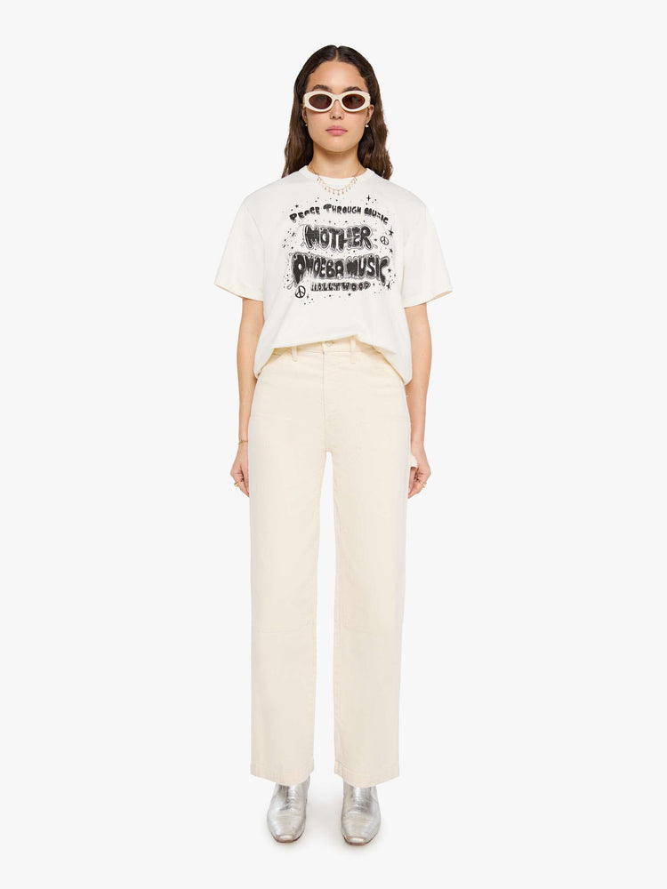 WOMAN full body view in a  white top with a MOTHER's spin on the classic Amoeba Music logo in black on the front.