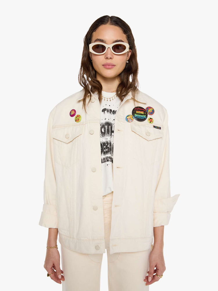 WOMAN front view in a  creamy white with tonal hardware, patches and pins denim jacket with drop shoulders, front patch pockets and a boxy fit.