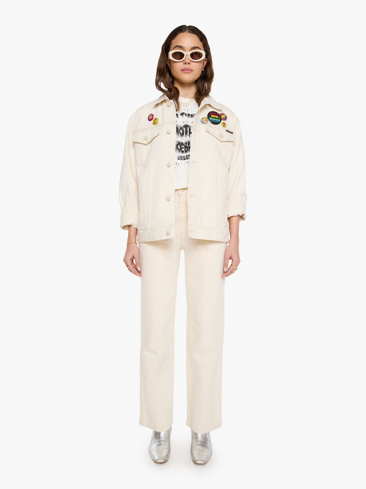 WOMAN full body view in a  creamy white with tonal hardware, patches and pins denim jacket with drop shoulders, front patch pockets and a boxy fit.