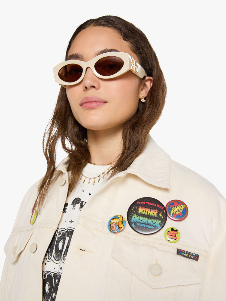 WOMAN close up view in a  creamy white with tonal hardware, patches and pins denim jacket with drop shoulders, front patch pockets and a boxy fit.