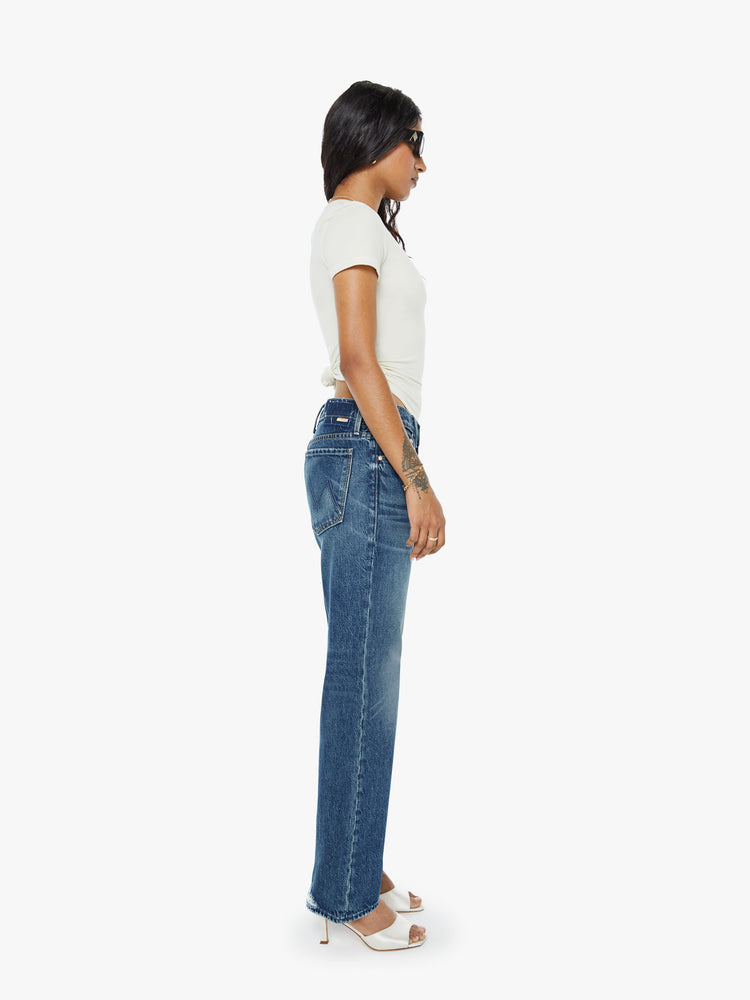 Side view of a petite woman in a  straight leg with a bit of a kick, the jean features a mid rise, full-length inseam and clean hem in a classic blue.