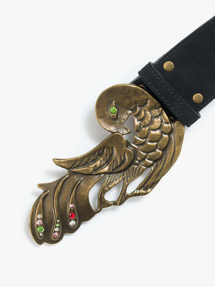 Close up view of a wide leather belt designed in black suede with an oversized antique brass buckle detailed with colored gemstones.