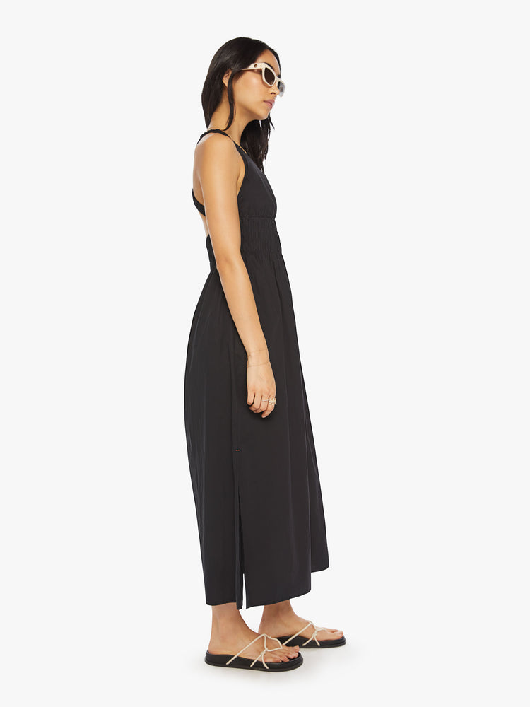 Side view of a woman maxi dress in black, sleeveless dress has a crew neck, thick gathered waistband and an ankle-grazing hem.