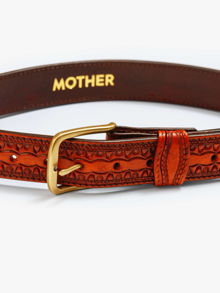 Close up flat view of a vintage-inspired leather belt with embossed and beaded details. 