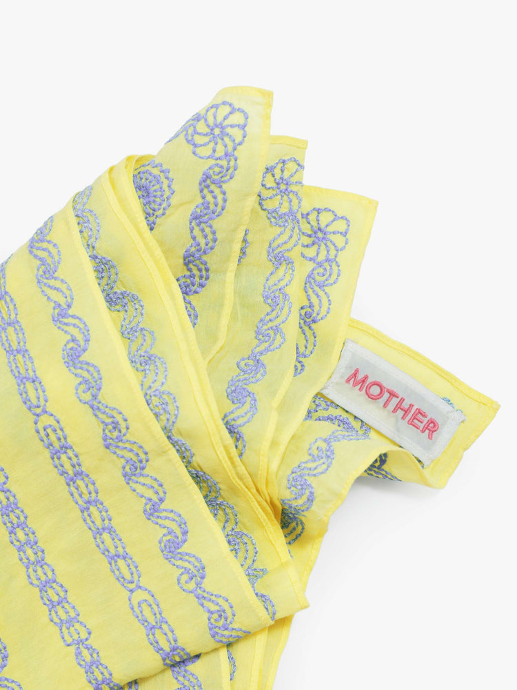 Folded flat of a 26" square scarf made from a cotton blend in pale yellow with piping-inspired embroidery in pink with baby blue trim.