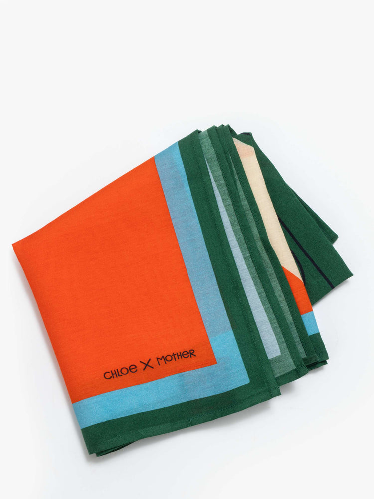Folded view of a red with green and blue trim square scarf can be worn as a neck tie, hair accessory or tied on a bag. 