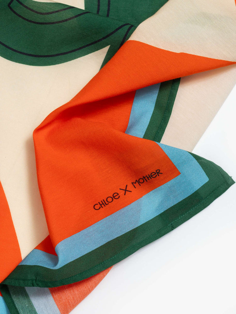 Close up view of a red with green and blue trim square scarf can be worn as a neck tie, hair accessory or tied on a bag. 