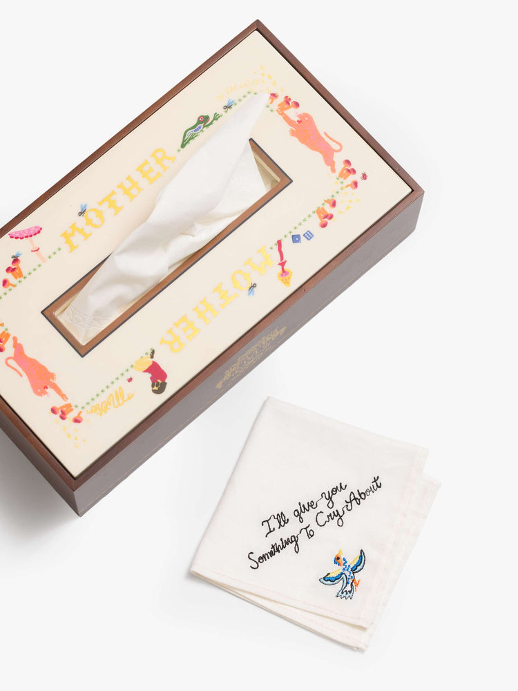A pine wood tissue box cover designed in brown and off-white with a vinyl-printed top featuring doodles and MOTHER's name in gold along the side with a tissue on the side.