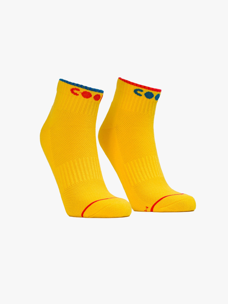 Front view of a pair of yellow ankle length socks with the word COOL in both red and blue.