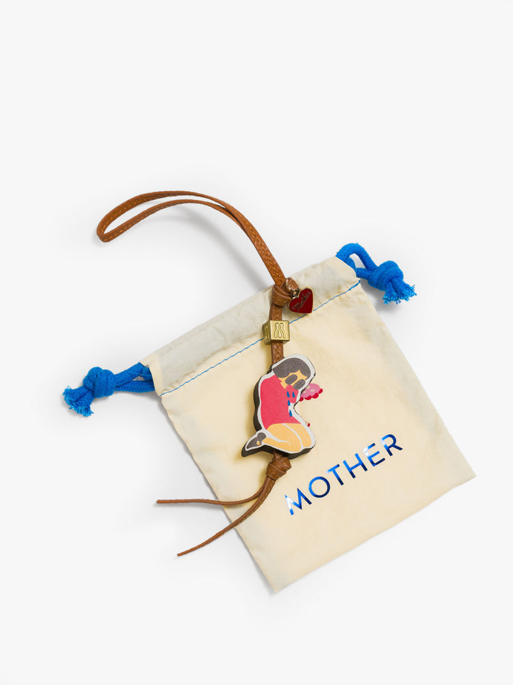 A tan bag charm made from 100% leather with a heart charm, M bead and a 1.8 x 1.4-inch crying girl at the end on top pf duster bag.