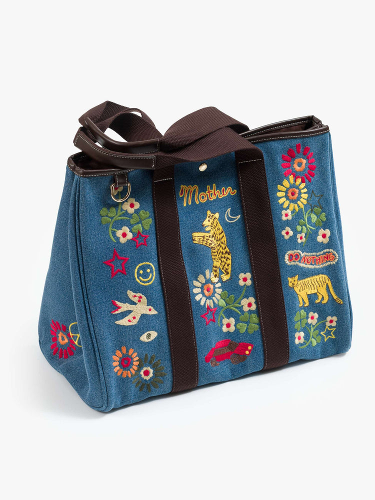 Side view of a Tote is designed in mid blue denim with brown top handles, colorful embroidery and MOTHER embroidered across the front in yellow and red.