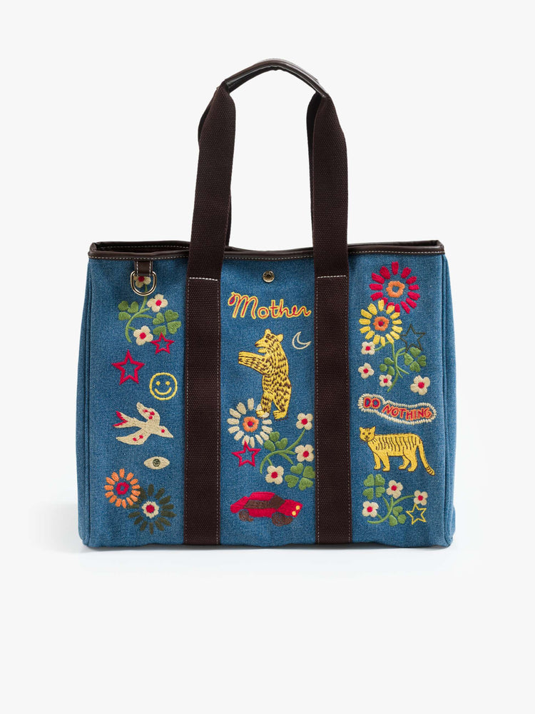Flat view of a Tote is designed in mid blue denim with brown top handles, colorful embroidery and MOTHER embroidered across the front in yellow and red.