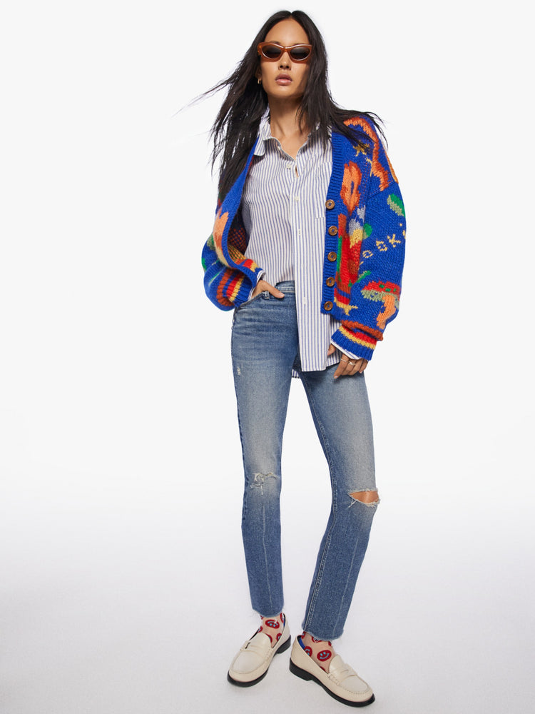 Editorial image of a model wearing medium blue wash denim jeans with distressed knees and a colorful cardigan.