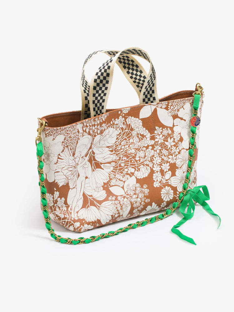 Front view of a leather purse with a white floral print, a pair of checkered handles, and a gold chain strap woven with green ribbon.