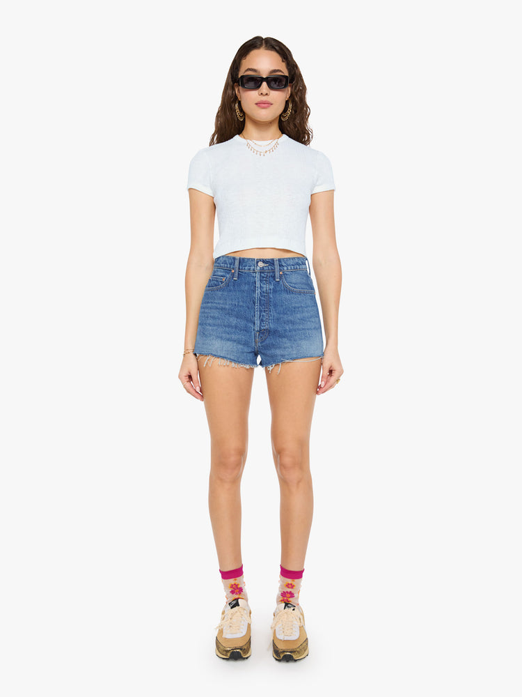 Front view of a woman in a super high-waisted denim shorts with a button fly, 2-inch inseam and a frayed hem in mid blue wash with cherries embroidered.
