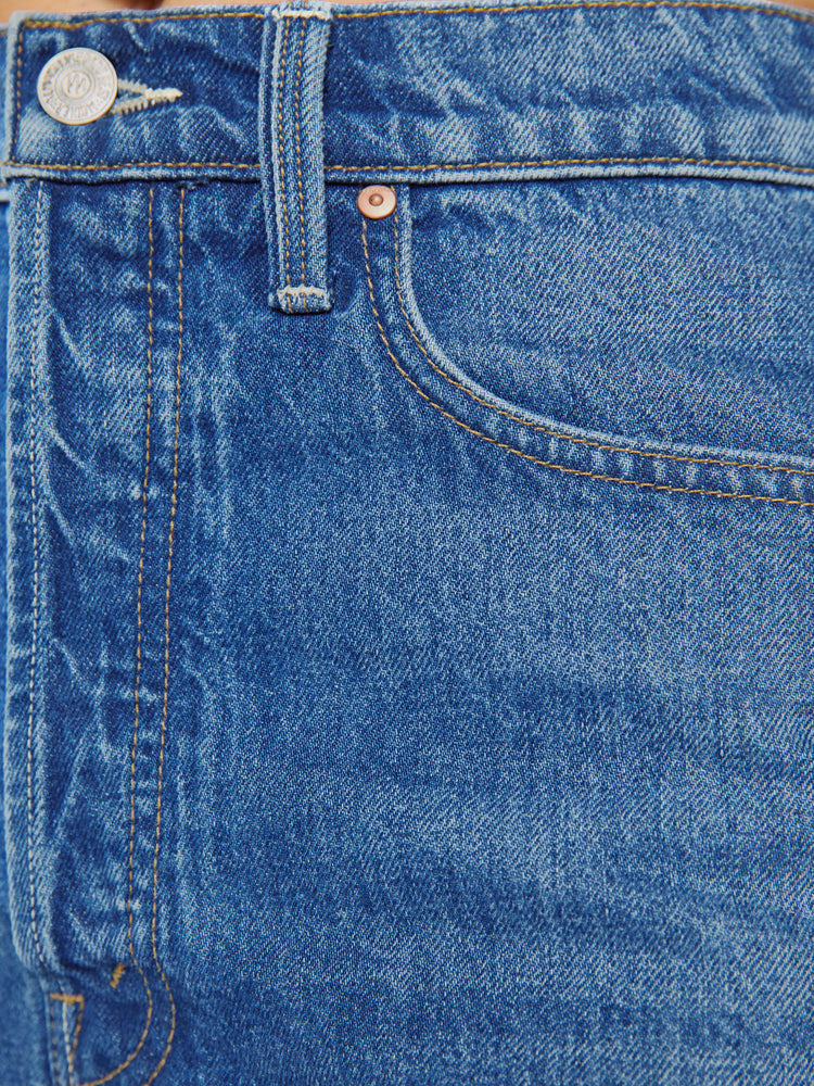 Close up view of a woman in a super high-waisted denim shorts with a button fly, 2-inch inseam and a frayed hem in mid blue wash with cherries embroidered.