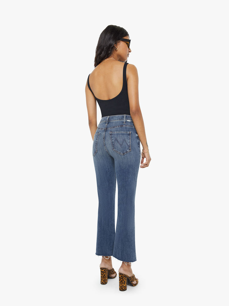 Back view of a petite woman mid blue wash jean with a high-rise flare has an ankle-length inseam and a raw hem.