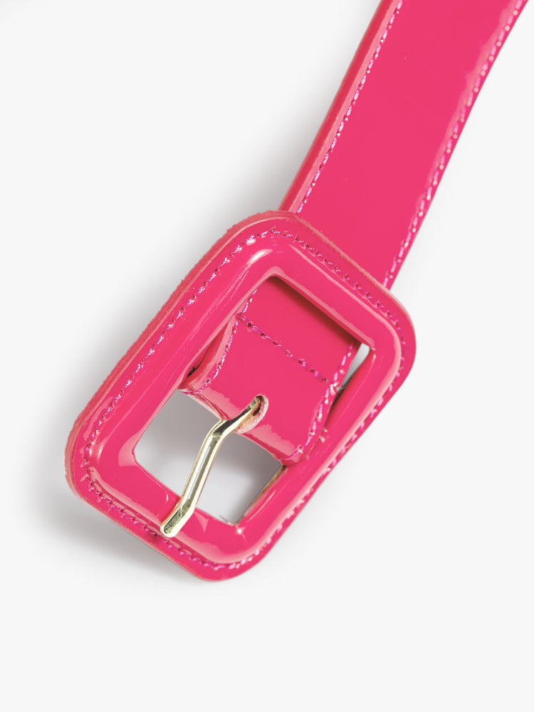 Close up view of a pink patent leather belt with an oversized square buckle. 