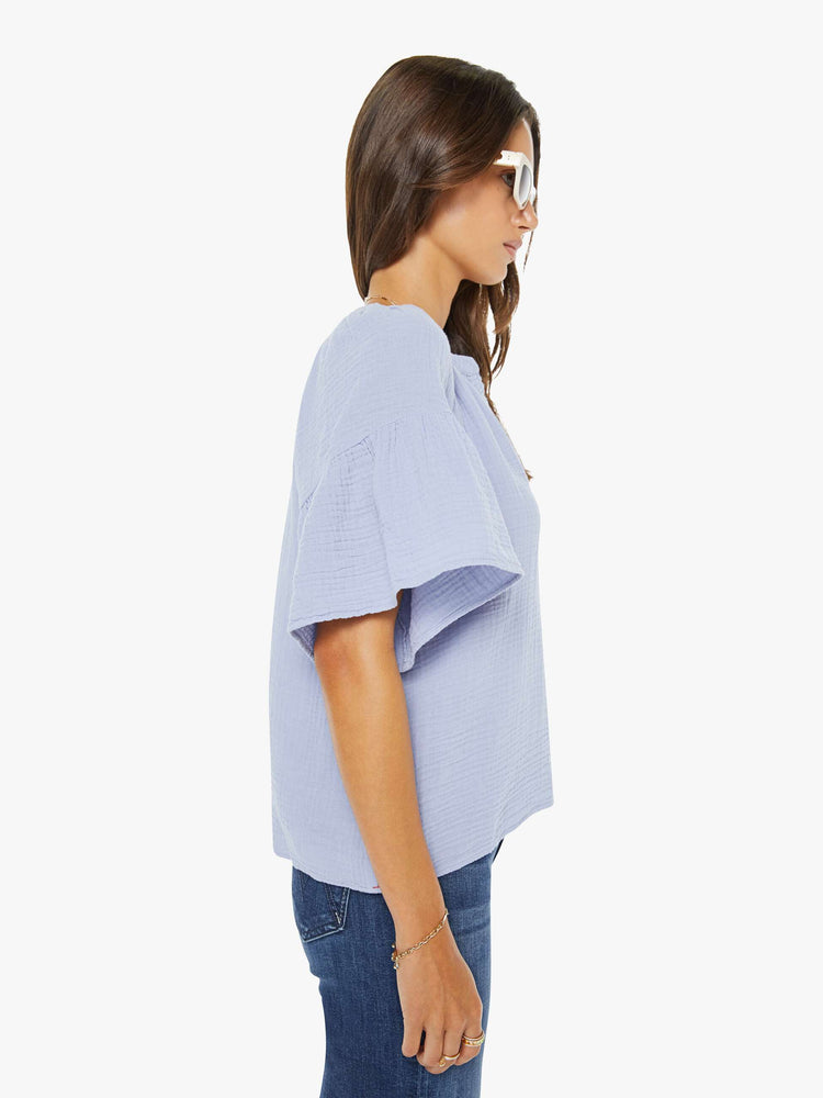 Side view of a woman in a light lavender with a deep V-neck, ruffled short sleeves and a loose, flowy fit.