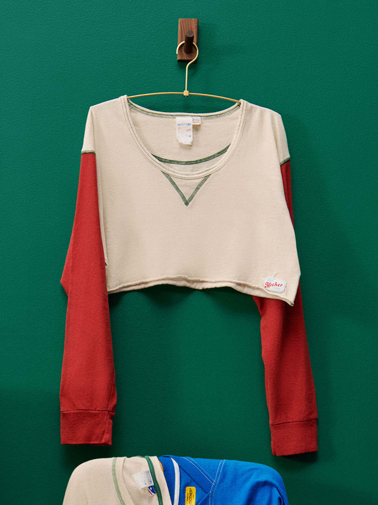 Lost & Found editorial image of a red and white cropped baseball tee, hanging against a green wall.
