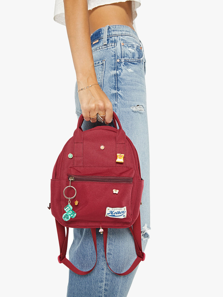 Side image of a woman holding a mini maroon backpack with assorted charms and a keychain.
