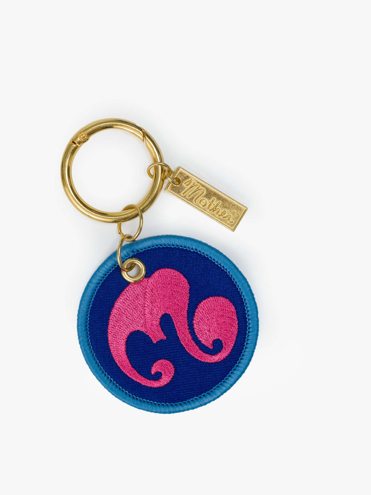 Back view of a gold-toned keychain with a circular M patch designed in blue and pink.