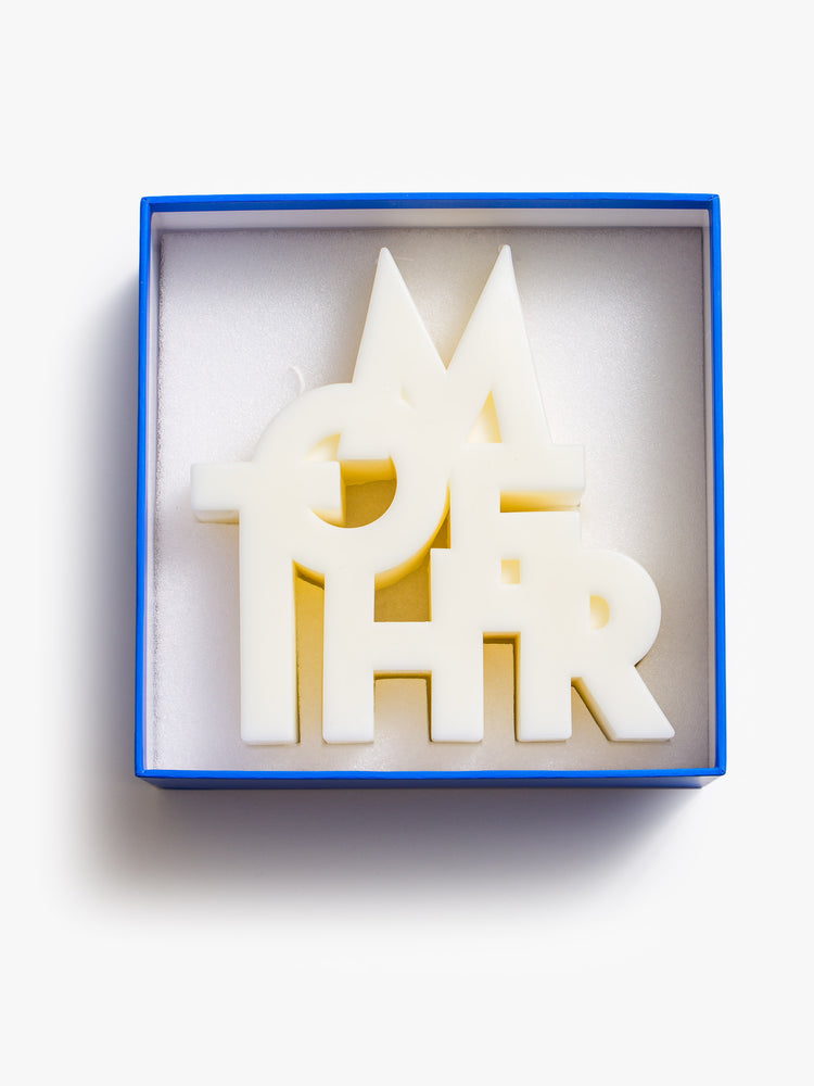 Image of an off white candle made up of stacked letters reading "MOTHER", inside a blue box..