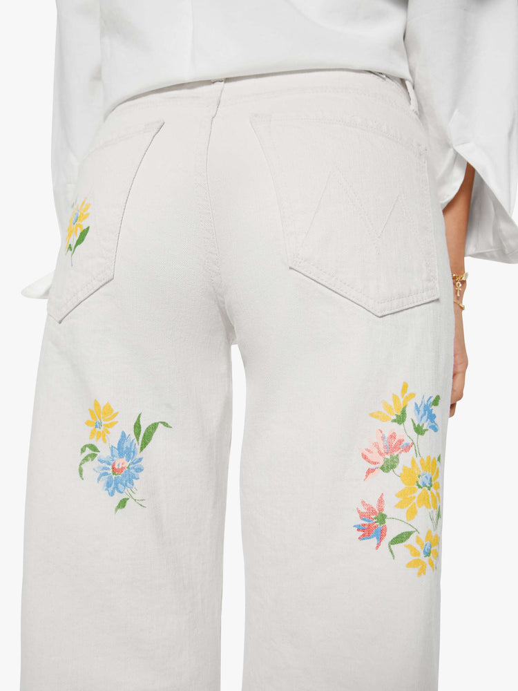 Close up view of a woman in a creamy white with floral print thoughout wide-leg jeans are designed to sit lower on the hips with a zip fly and clean ankle-length inseam.
