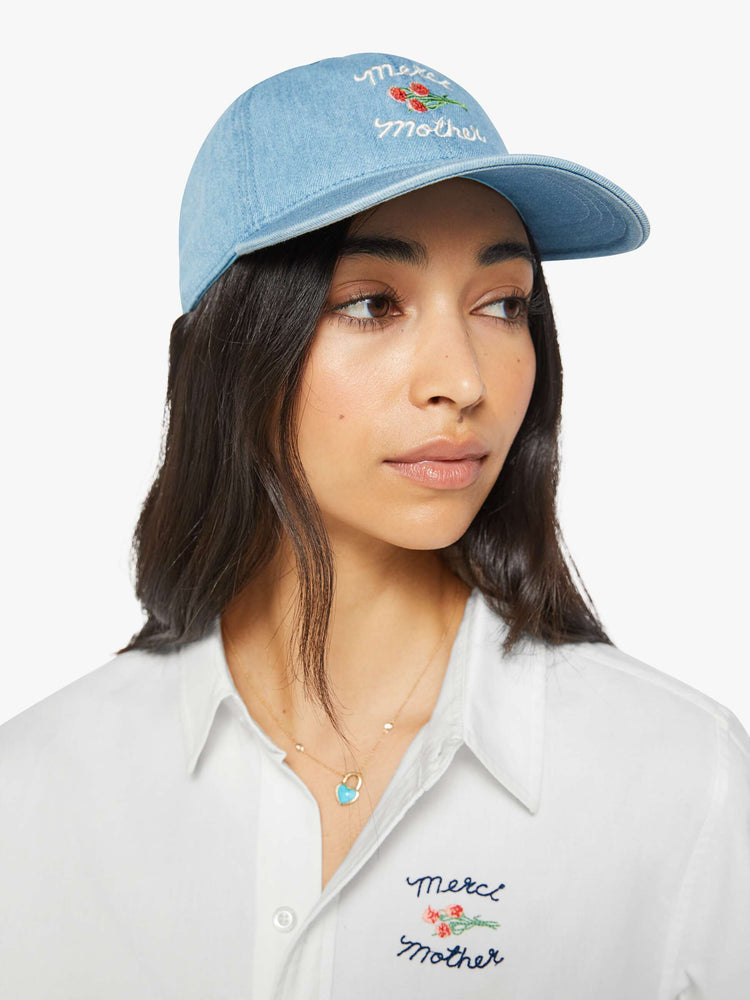 On model view of a light denim hat with embroidered text in white and a bouquet of red flowers.