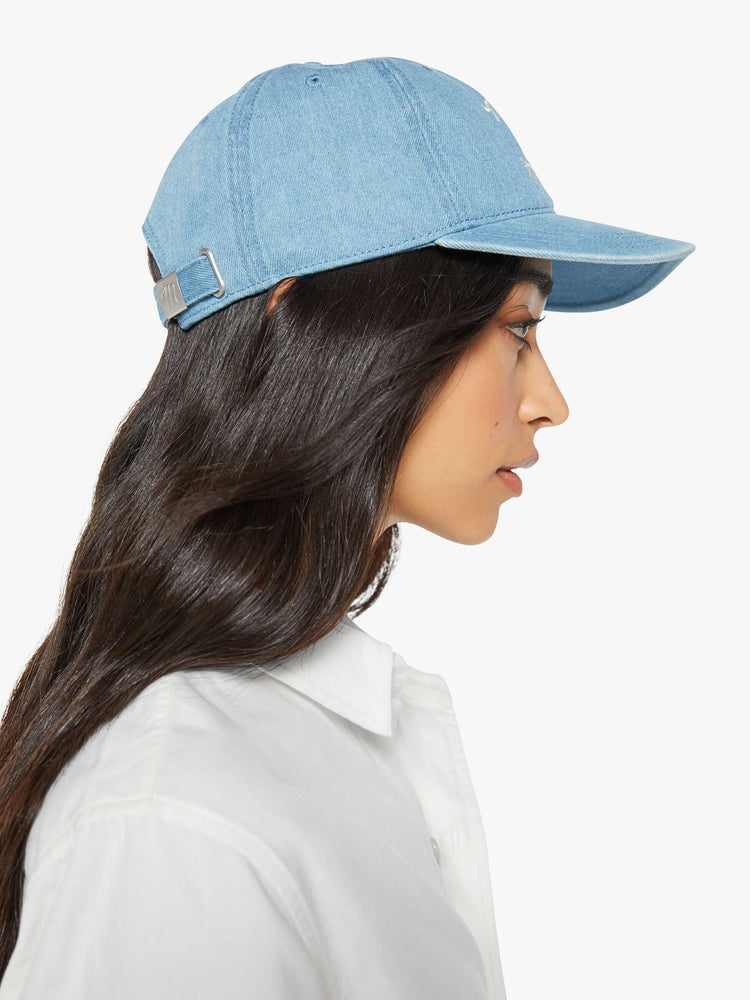 Side on model view of a light denim hat with embroidered text in white and a bouquet of red flowers.
