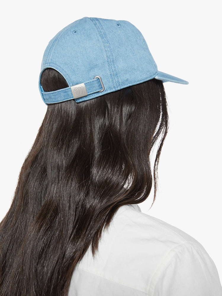 Back on model view of a light denim hat with embroidered text in white and a bouquet of red flowers.