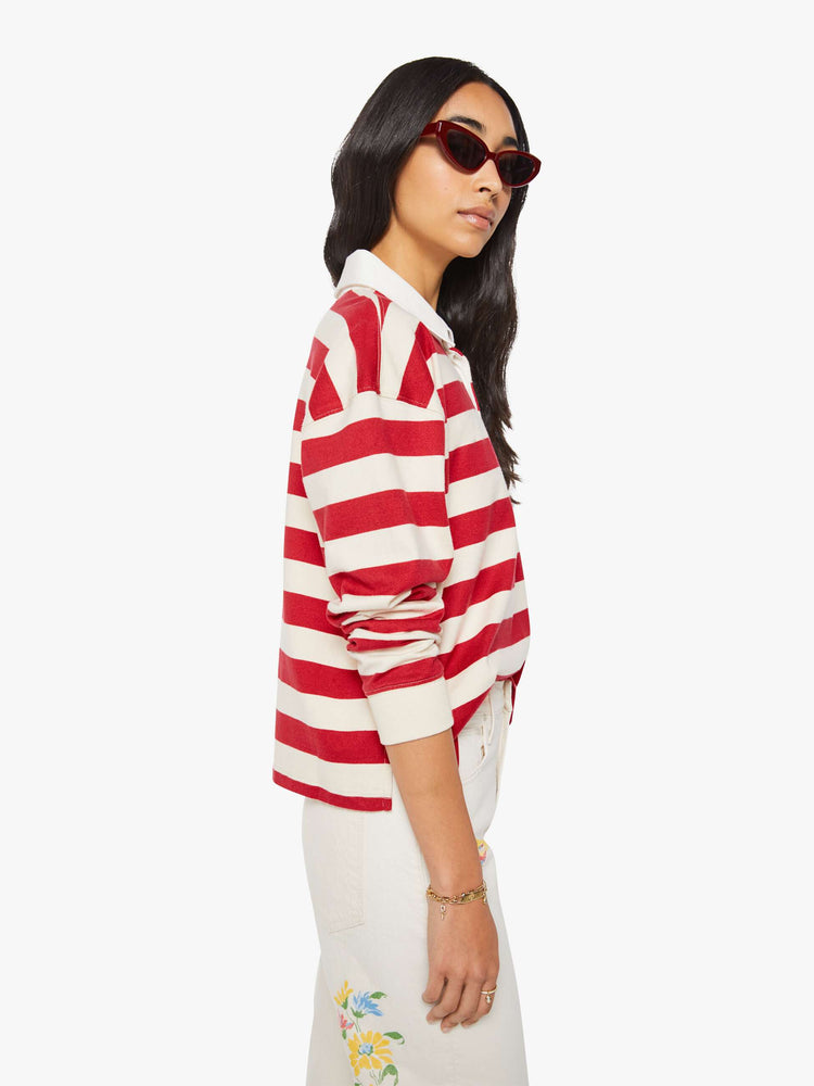 Side view of a woman in a long-sleeve top in off-white and red stripes with embroidered text in navy and a small bouquet on the chest.