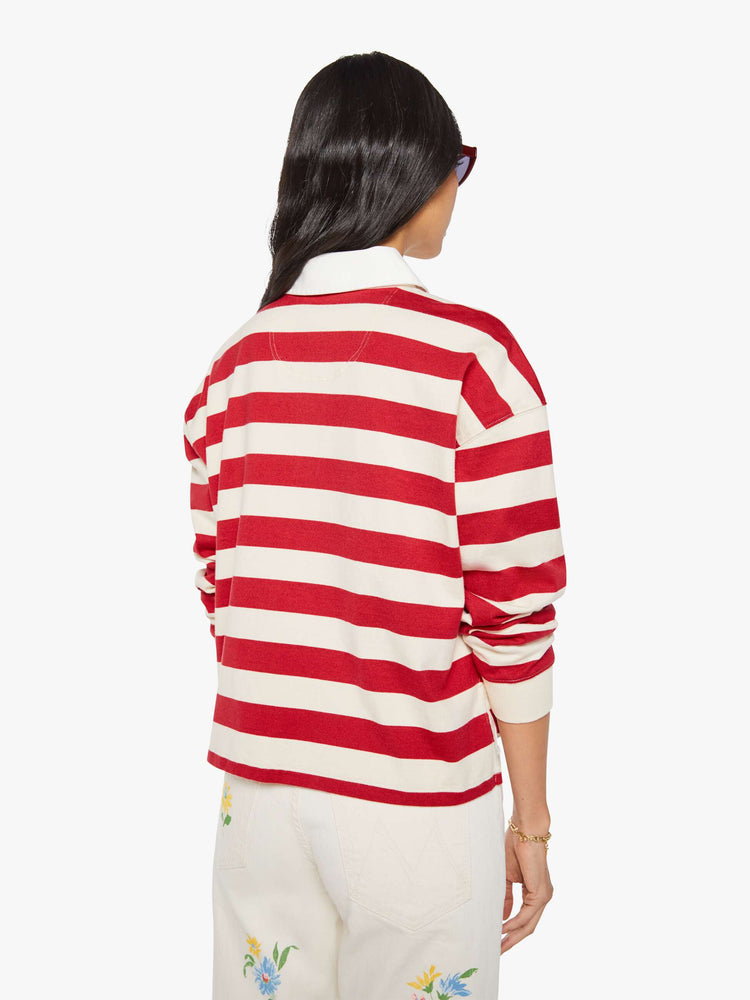Back view of a woman in a long-sleeve top in off-white and red stripes with embroidered text in navy and a small bouquet on the chest.