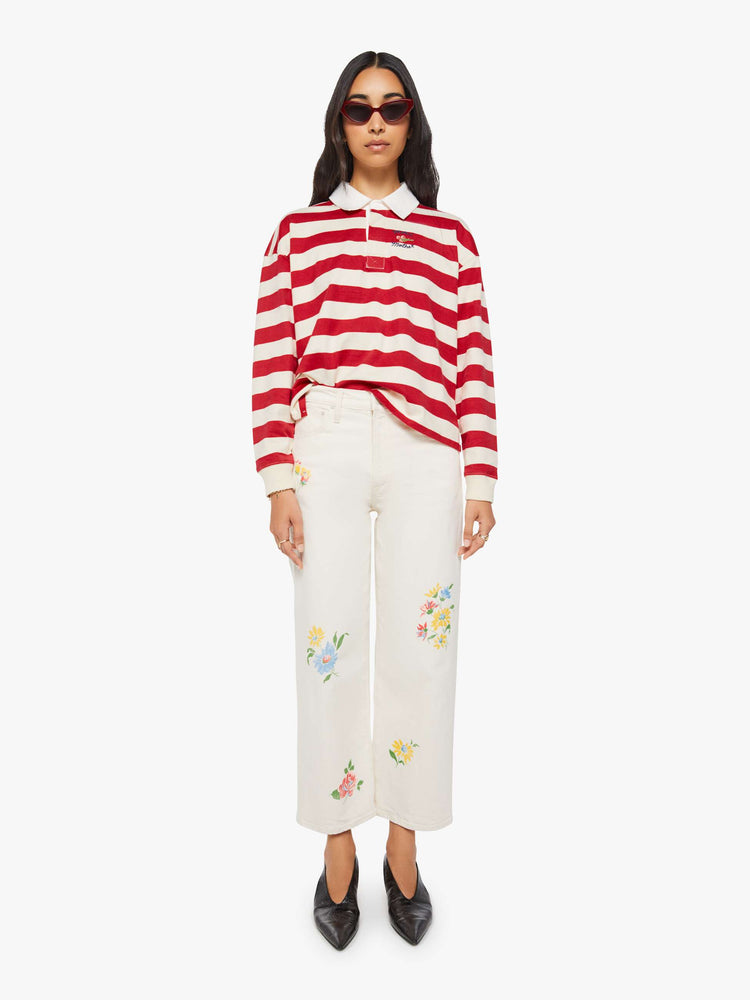 Full body view of a woman in a long-sleeve top in off-white and red stripes with embroidered text in navy and a small bouquet on the chest.