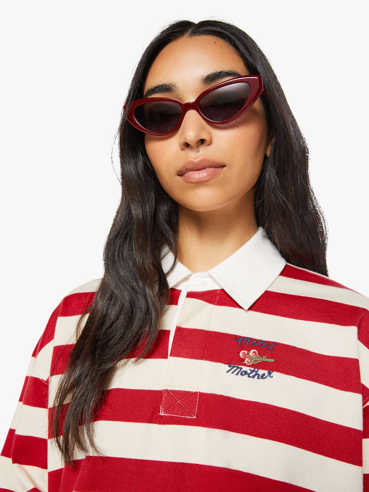 Close up view of a woman in a long-sleeve top in off-white and red stripes with embroidered text in navy and a small bouquet on the chest.