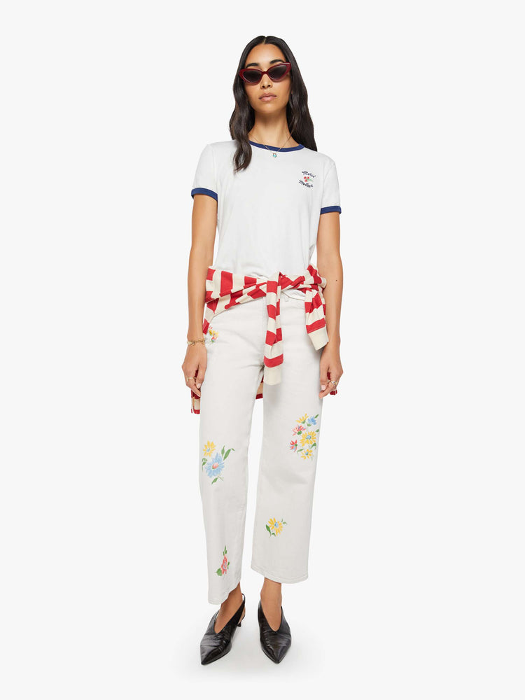 Full body view of a woman in a short sleeve tee is made from 100% supima cotton in white with navy trim, and features embroidered text in navy and a small bouquet on the chest.