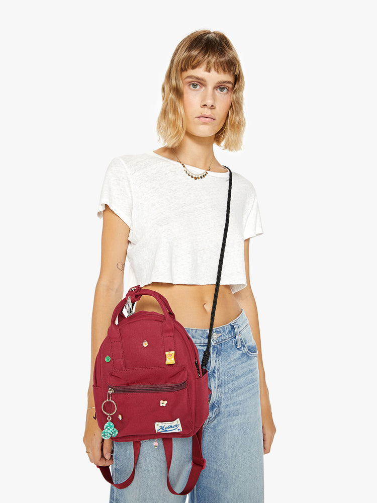 Front image of a woman wearing a mini maroon backpack with assorted charms and a keychain.