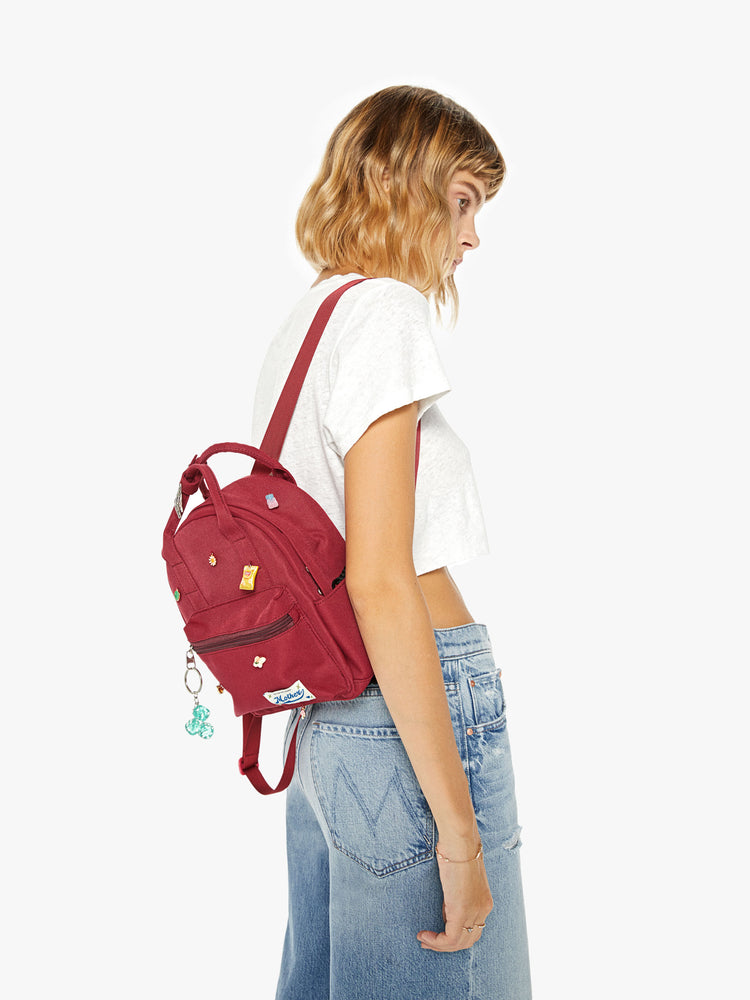 Back image of a woman wearing a mini maroon backpack with assorted charms and a keychain.