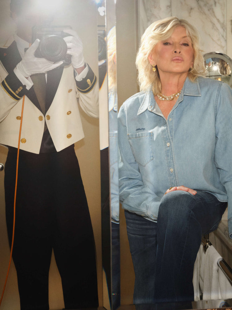 Martha standing in front of a hotel bathroom mirror, wearing a light blue chambray Mother shirt and dark blue denim.