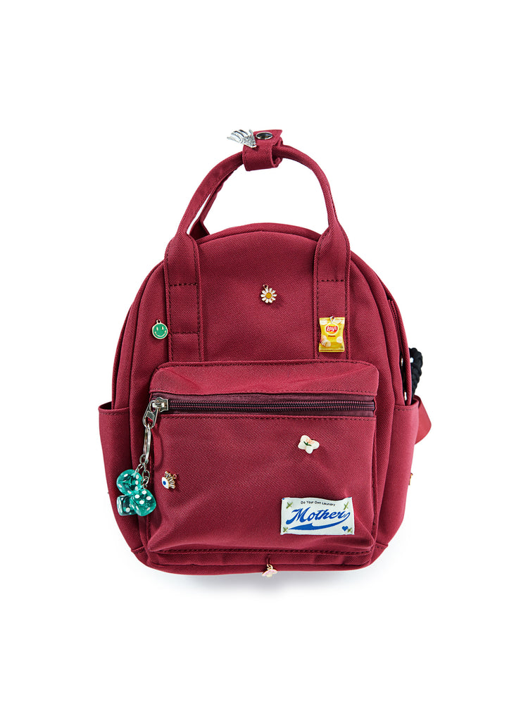 Flat of a maroon backpack featuring assorted charms and a dice keychain.
