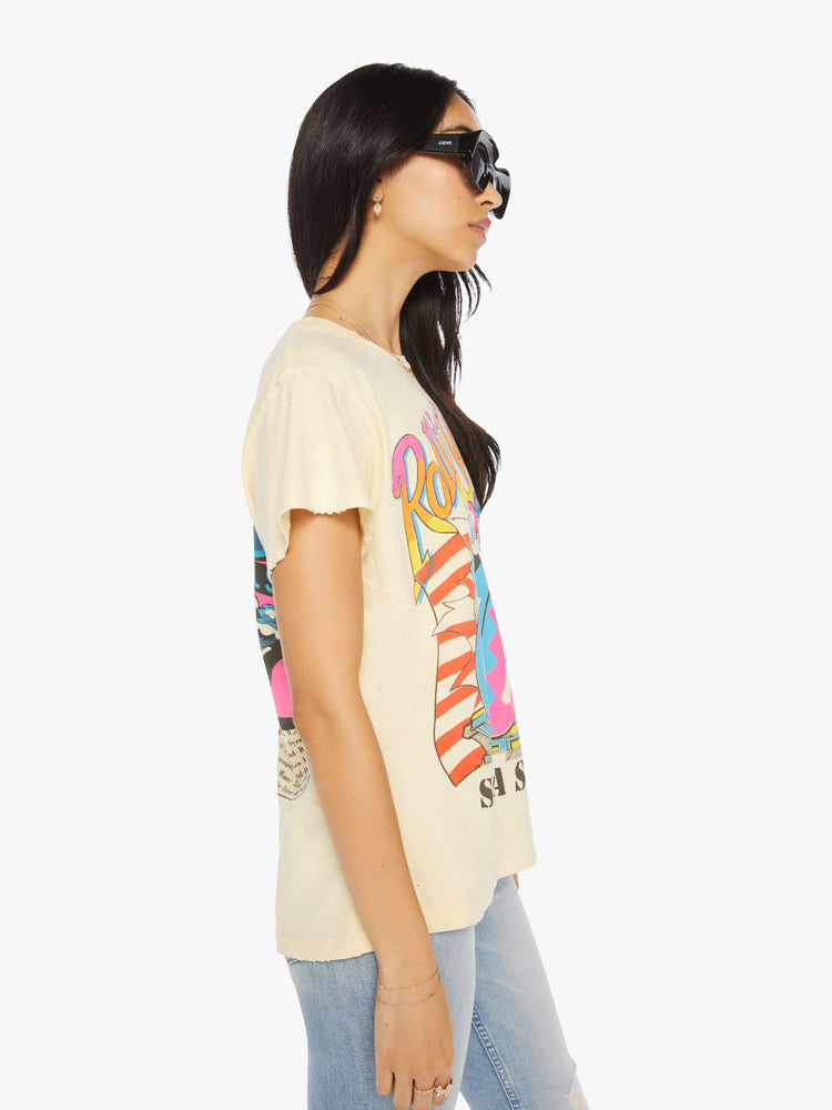 Side view of a woman hand distressed crewneck tee in a pastel yellow hue the tee riffs on the Rolling Stones' Steel Wheels tour with the band's iconic tongue-and-lips logo on the front and tour dates on the back.