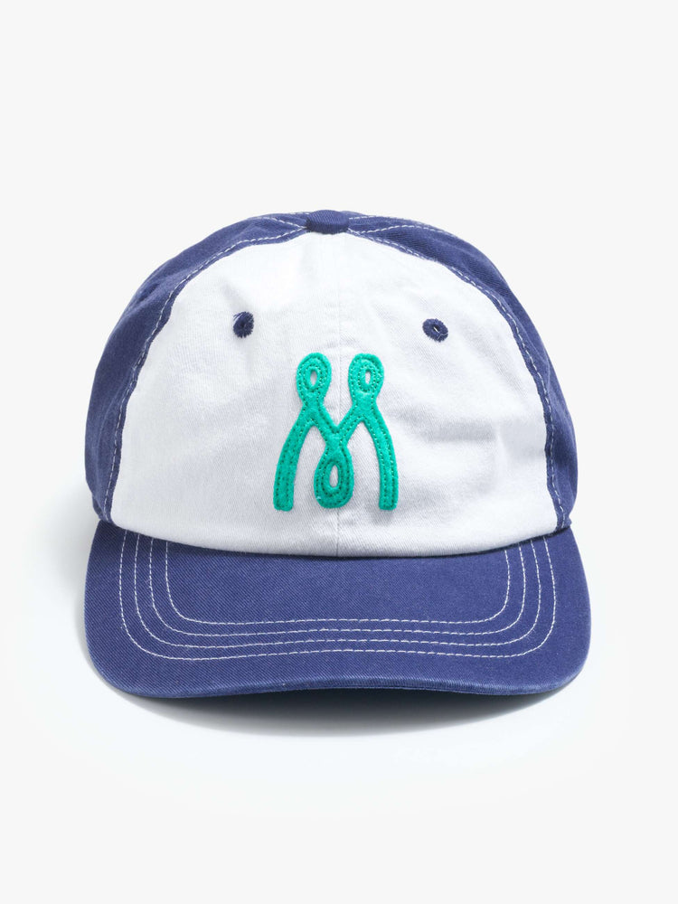 Flat view of a woman dad hat designed in white and navy 100% cotton with white stitching and an M embroidered in teal on the front.