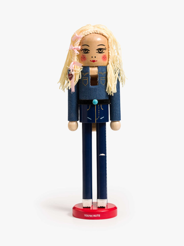 Front view of a traditional nutcracker a 70s-inspired twist with a Canadian tuxedo, turquoise-detailed belt, blonde braids, pink bows and a MOTHER heart charm.