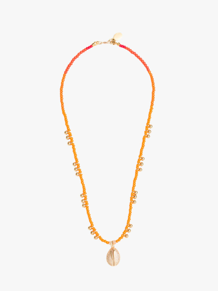 View of a beaded necklace features orange seed beads, brass balls and a gold-plated shell charm.