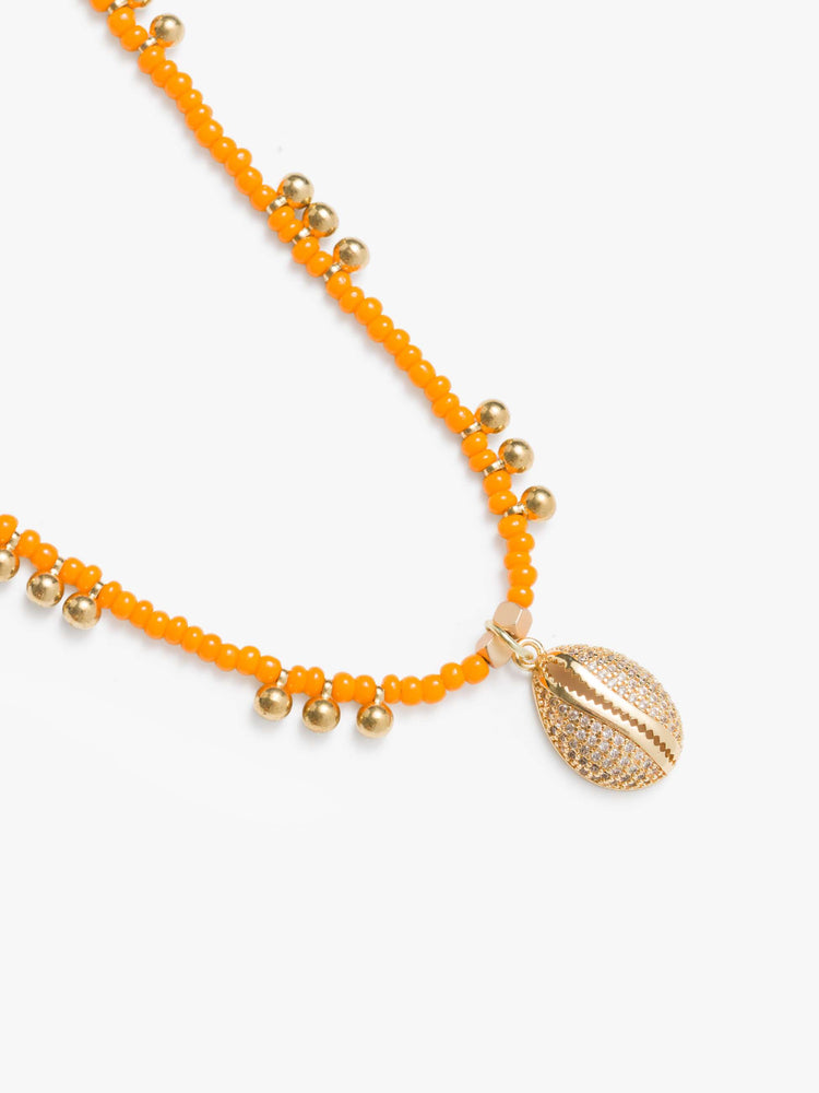 Close up view of a beaded necklace features orange seed beads, brass balls and a gold-plated shell charm.