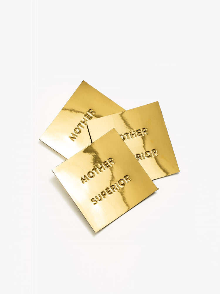 A pile of metallic gold square MOTHER SUPERIOR labels.