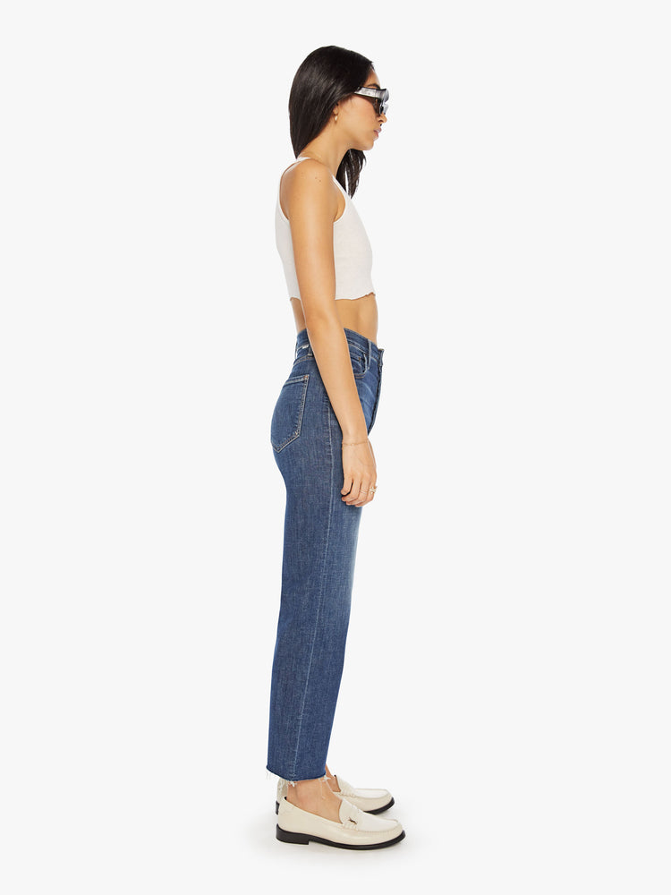 Side view of a womens dark blue denim jean featuring a high rise, a wide straight leg, and ankle length raw hem.